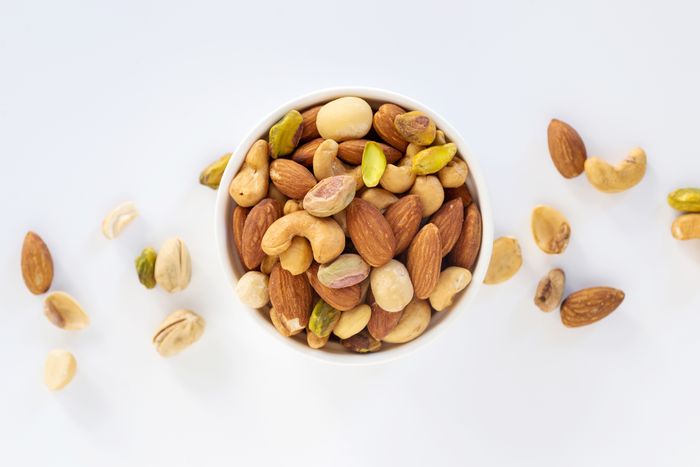 An overhead shot of a white bowl of mixed nuts on a white background.